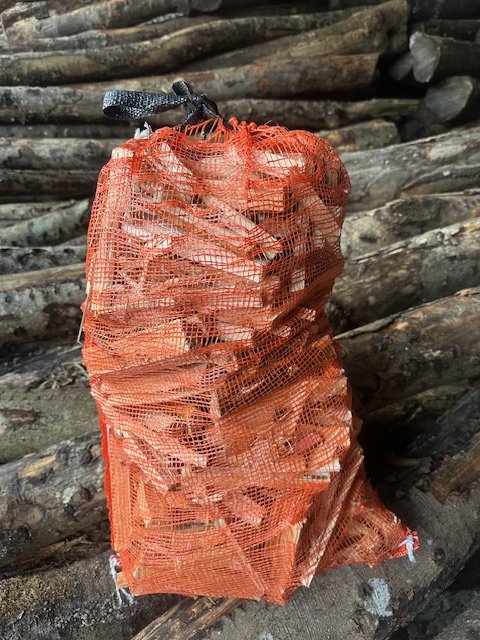 An extra-large orange net of dry kindling propped against a stack of split logs